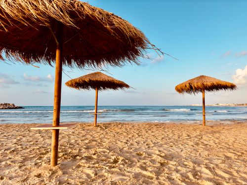 Free A tranquil beach scene in Gournes Gouvon, Greece with natural straw umbrellas and calm sea waves. Stock Photo