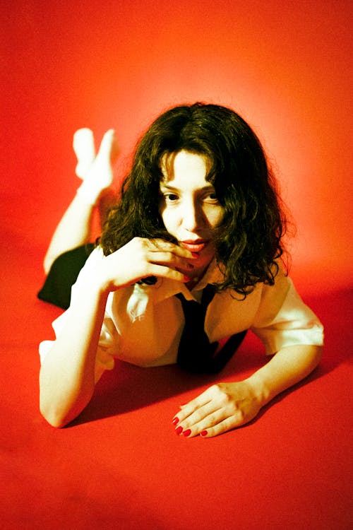 A woman laying down on a red background with her hands on her head