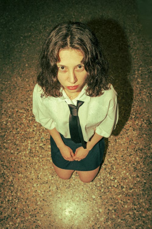 A woman in a tie and skirt kneeling on the floor