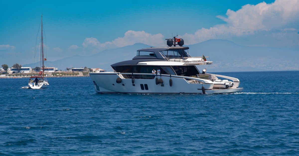 A luxury yacht sails in Foça, İzmir, Türkiye, under clear summer skies.