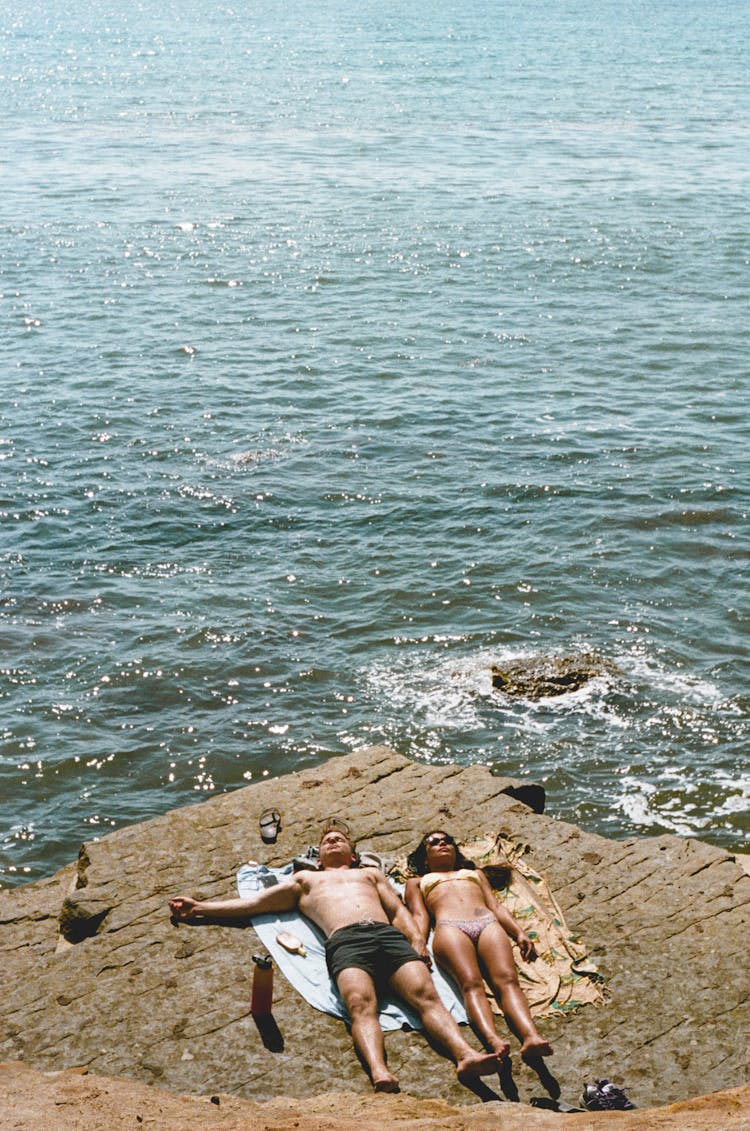 Photo Of Couple Lying Down On Cliff Near Sea