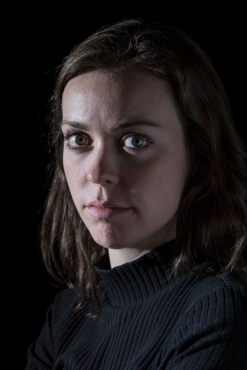 Free Close-up portrait of a serious young woman with brunette hair in a dark studio setting. Stock Photo