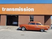 在一个阳光明媚的日子里，一辆闪亮的橙色老爷车停在变速箱维修店外