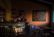 这家温暖的酒吧内设有一个色彩缤纷的柜台和凳子，与调酒师工作区旁充满活力的艺术品相映成趣
