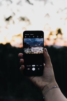 A person captures a scenic sunset using a smartphone, emphasizing modern mobile photography.