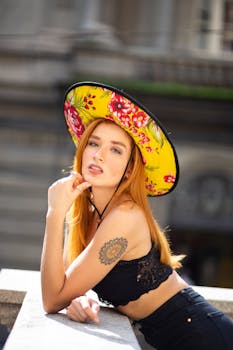 一位红发时尚女性在户外戴着一顶充满活力的花卉帽子摆姿势，展示她的纹身