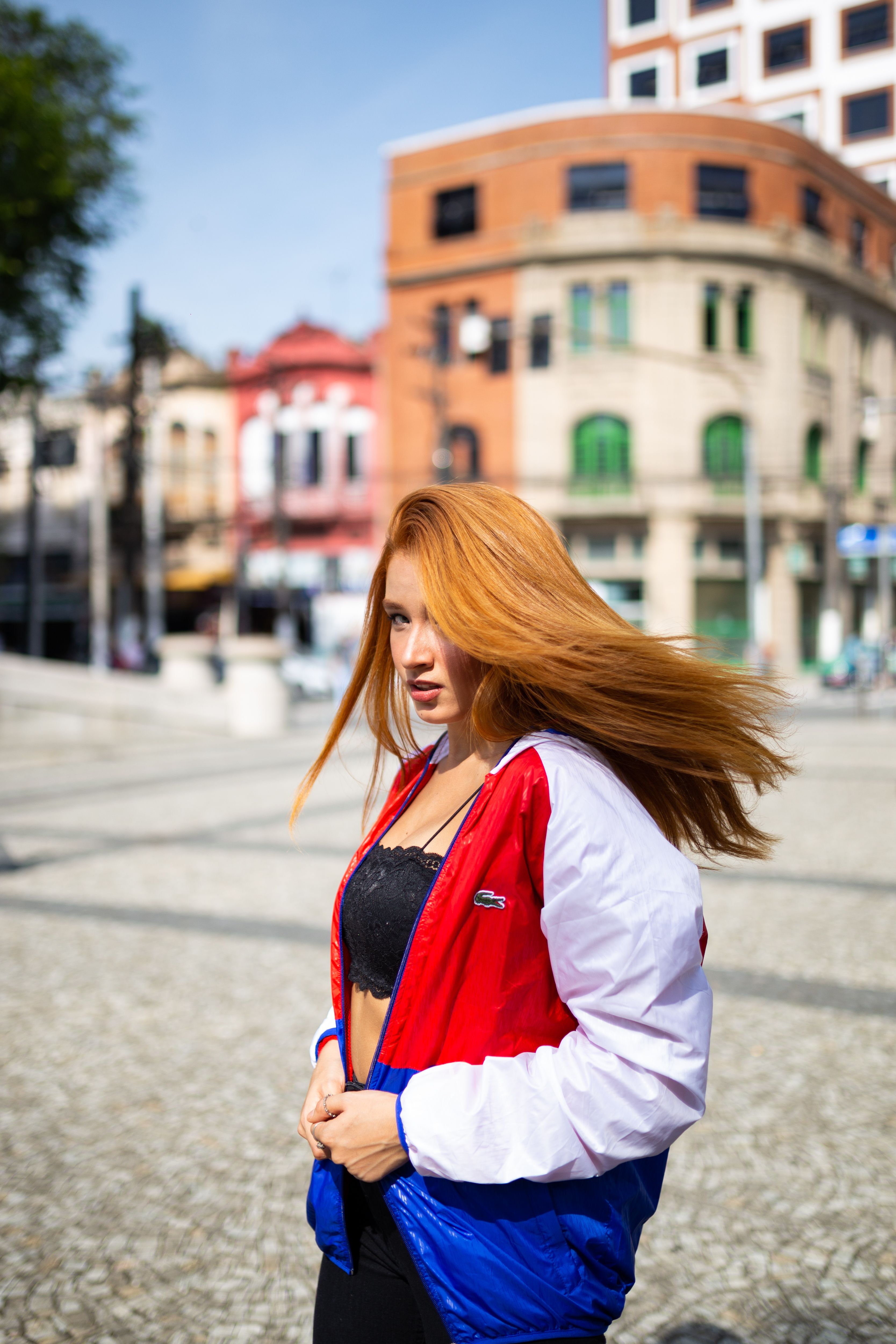 Stylish woman poses with dynamic hair flip in a vibrant Santos cityscape.