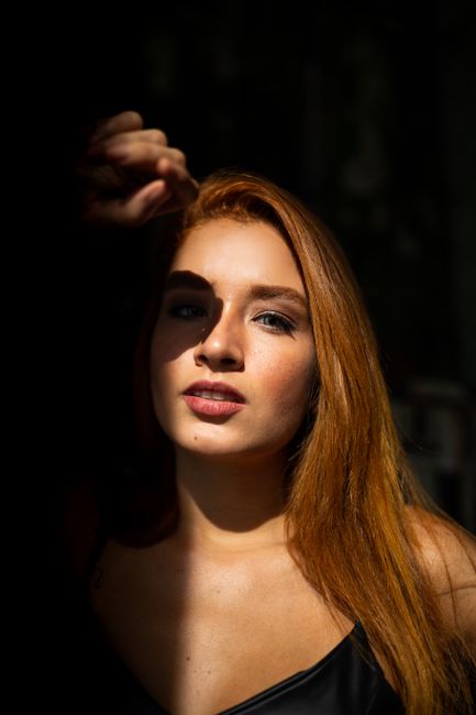 Captivating portrait of a young woman with red hair, featuring dramatic light and shadows.