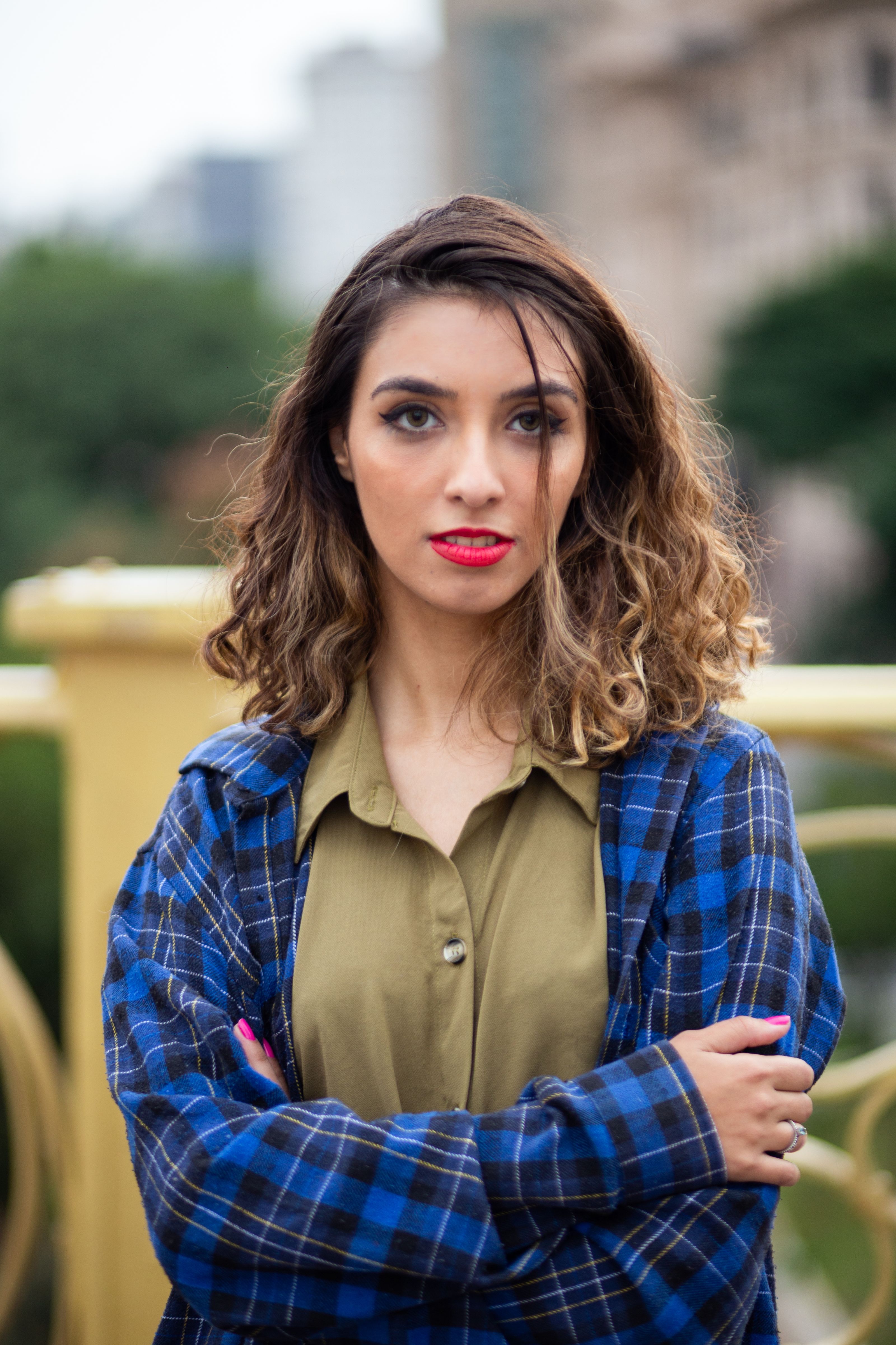 Jovem mulher com lábios vermelhos e camisa xadrez posando confiantemente ao ar livre em São Paulo.