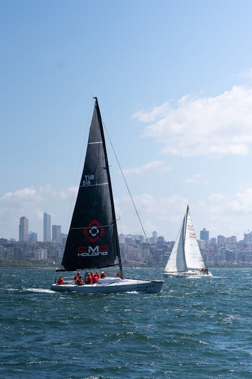 Two sailboats are sailing in the water with a city in the background