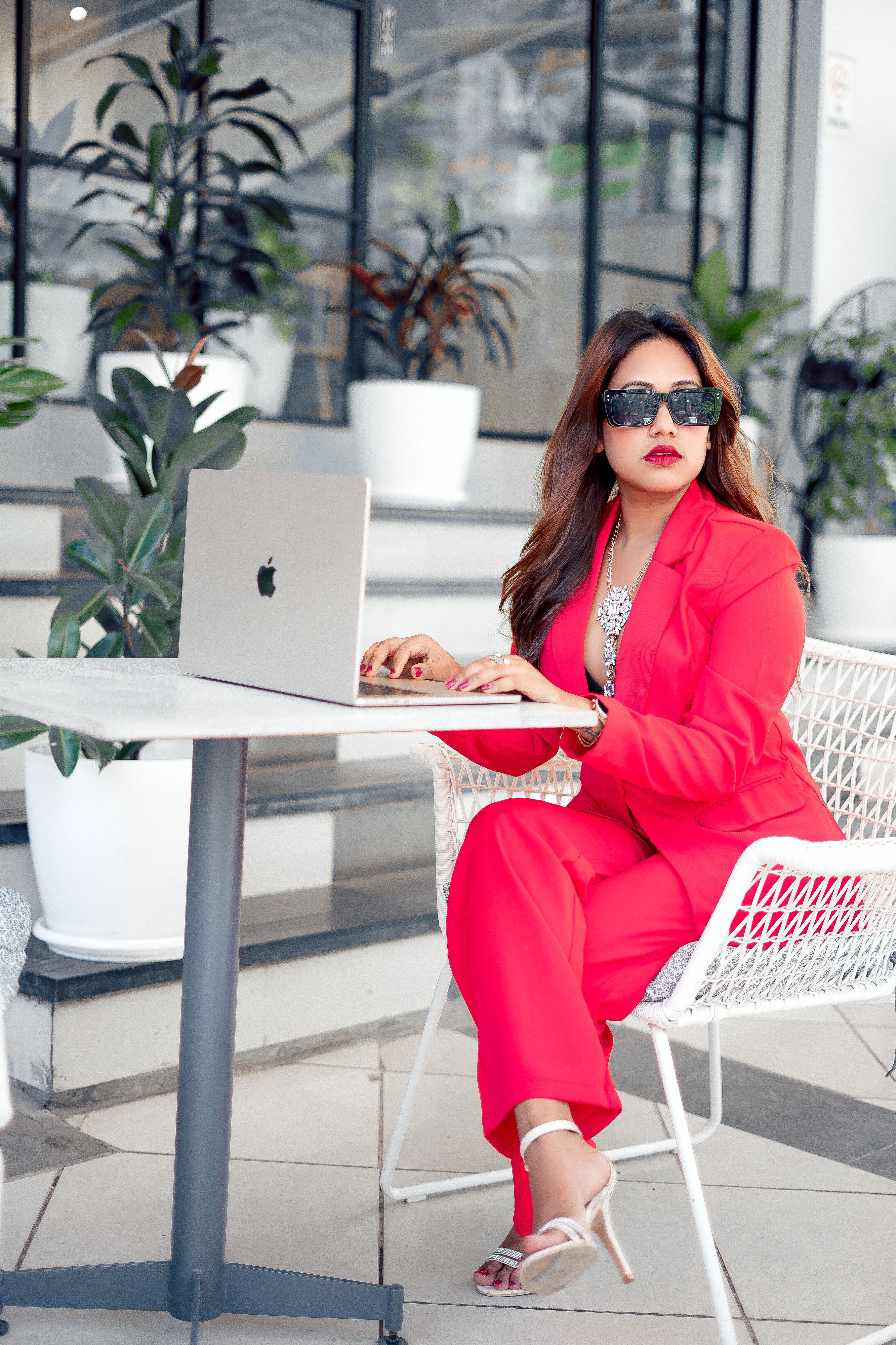 Stylish woman in vibrant red suit using a laptop at a modern outdoor cafe.