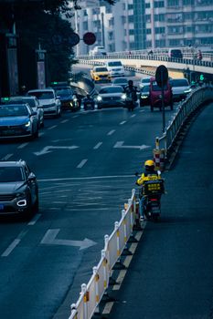 A delivery person riding a scooter on a busy street in Luzhou, China.
