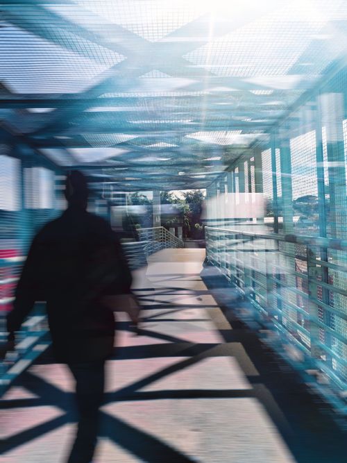 Free Blurred silhouette of a person walking on a modern footbridge with geometric shadows in urban setting. Stock Photo