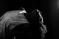 African American female in white sleeveless shirt with curly hair tilting back in darkness