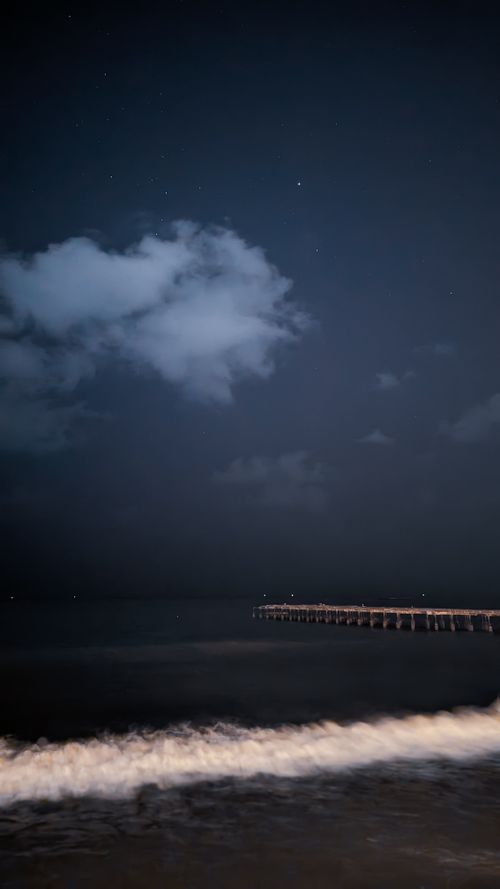 Free Serene nocturnal scene of a pier stretching over the calm ocean under a starlit sky. Stock Photo