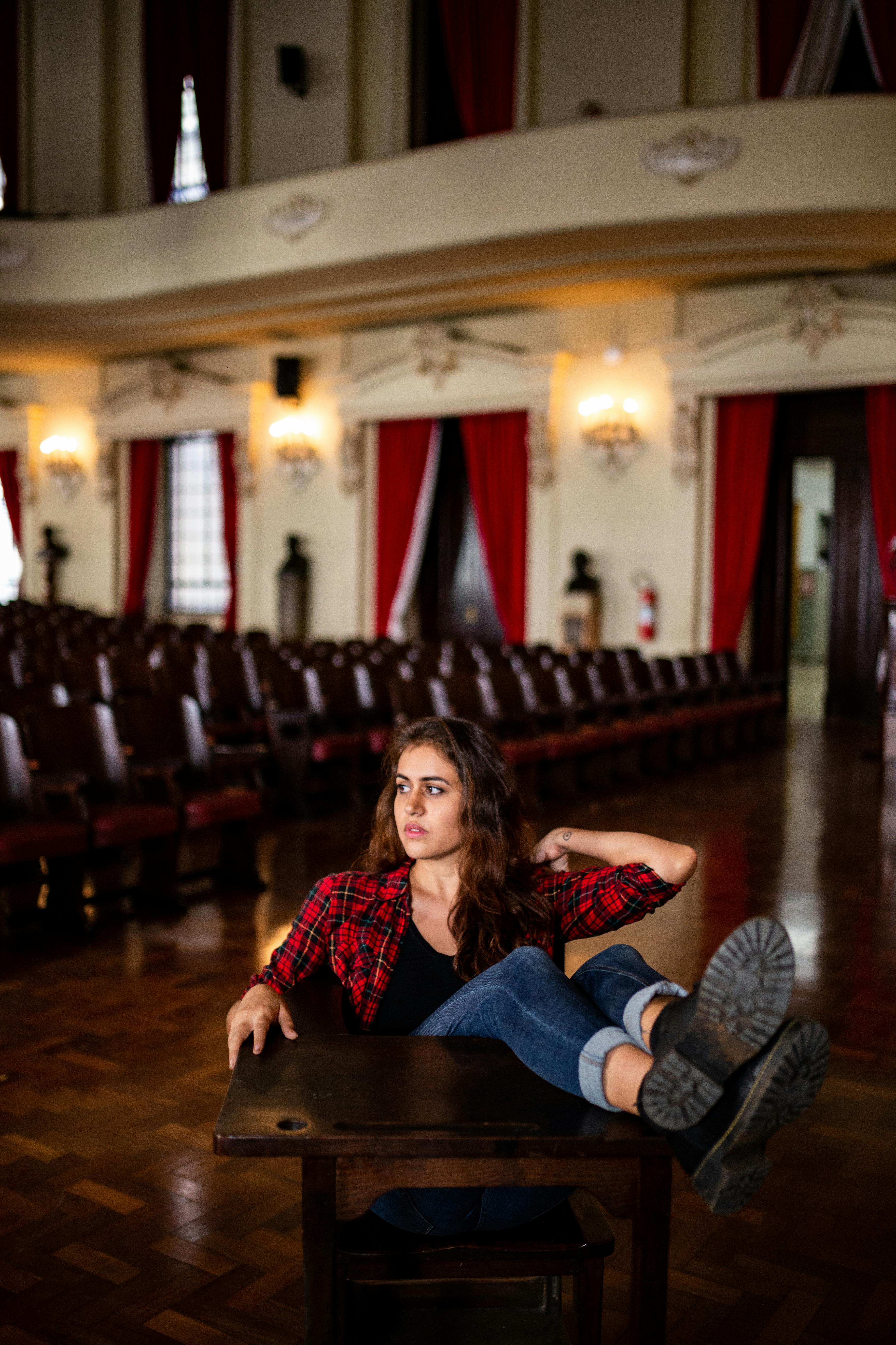 Free Young woman in red plaid shirt relaxing on chair in ornate theater hall. Stock Photo