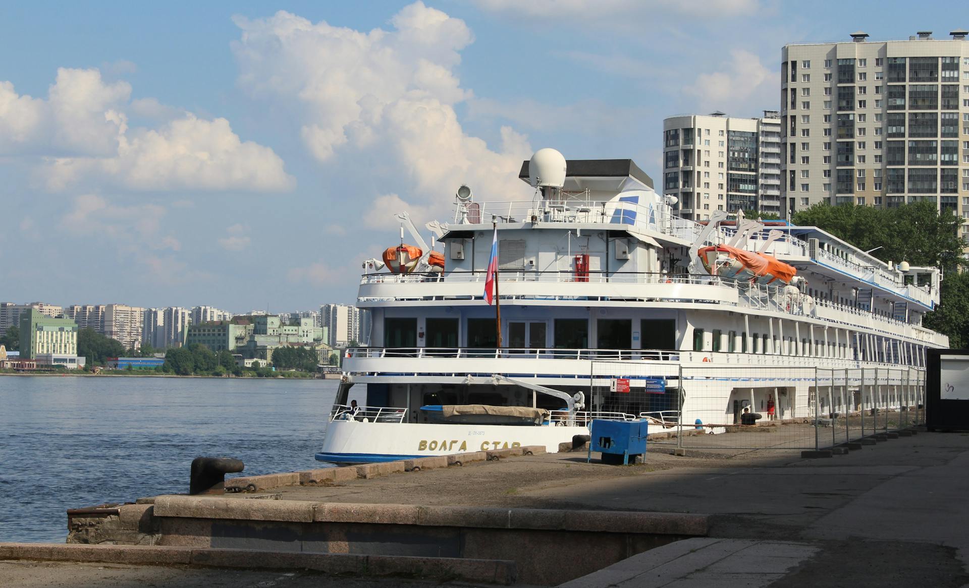 Cruise ship docked at a city harbor, against a backdrop of urban high-rise buildings.