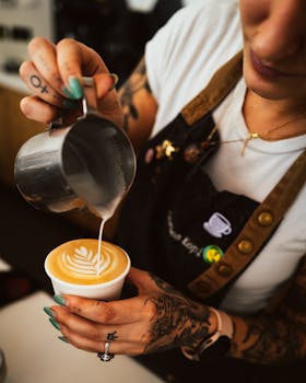 A barista pours milk to craft a latte art design in a coffee shop.
