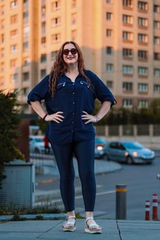 Smiling woman in urban attire standing confidently on city street in evening light.