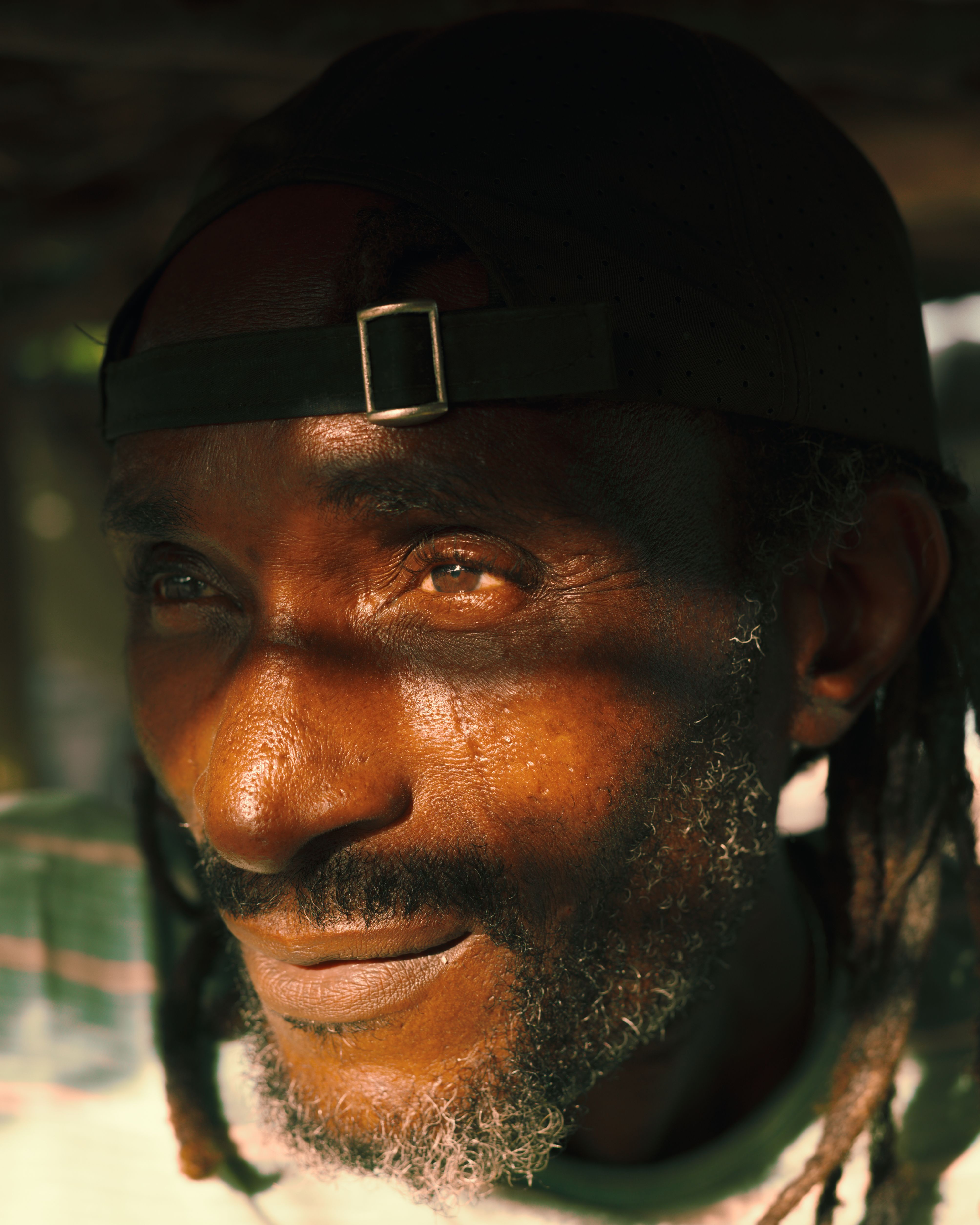 Close-up portrait of a smiling man with a cap and beard, warmly lit by sunlight in Lagos.