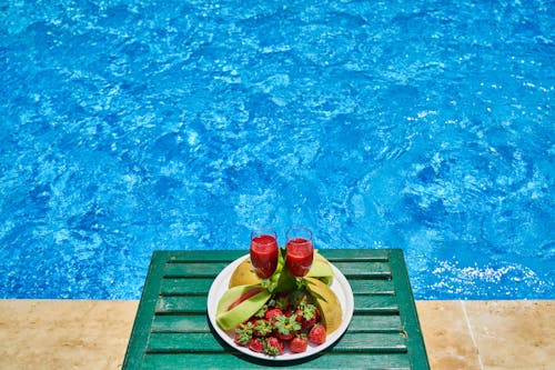 Dois Copos De Bebida E Um Prato De Frutas à Beira Da Piscina