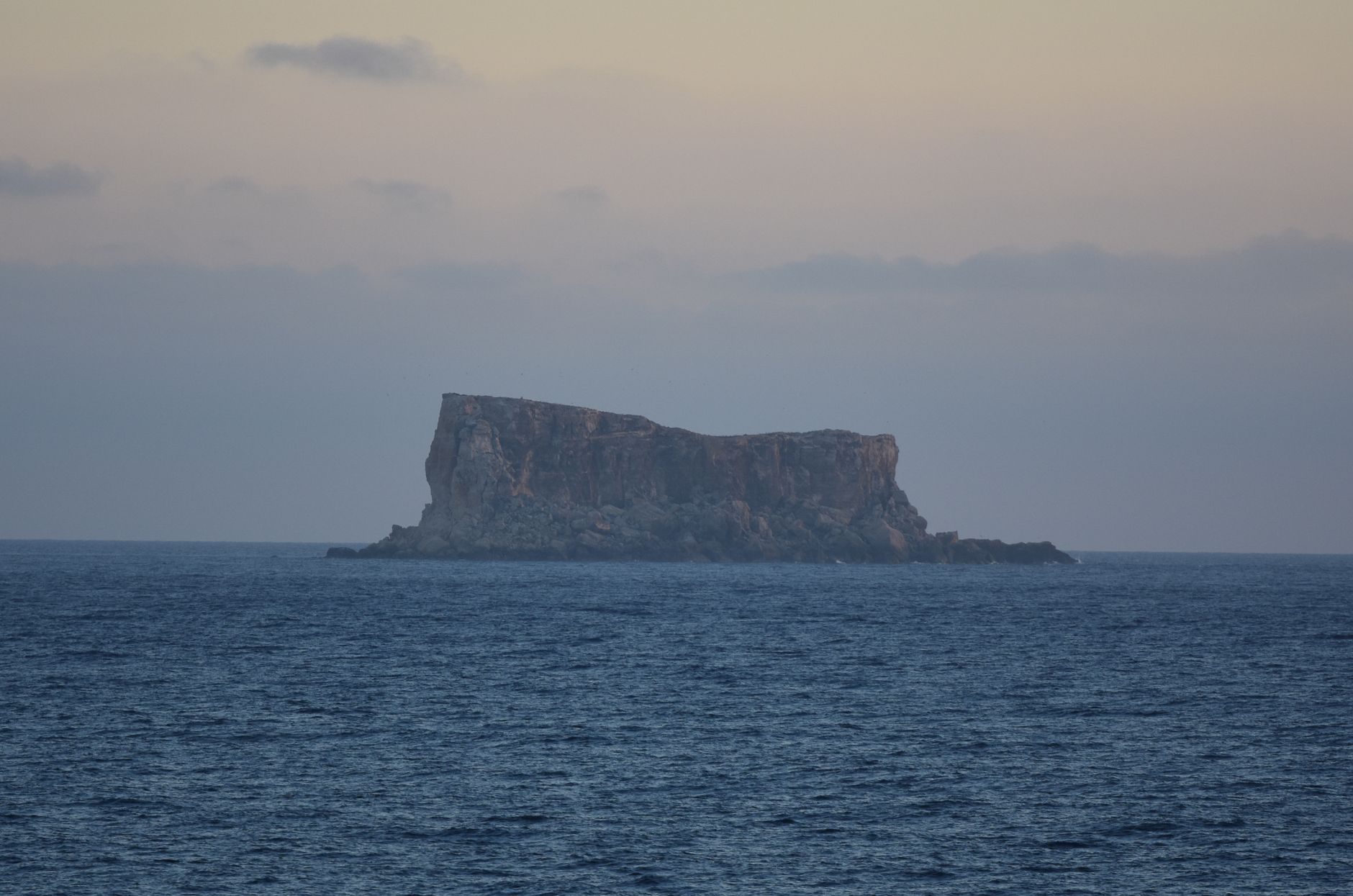 Serene view of a misty island cliff surrounded by calm sea waters at twilight.