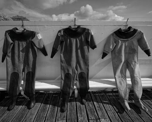 Three black and white photos of diving suits hanging on a dock
