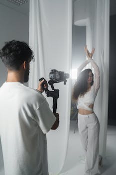 A photographer captures a model during a studio fashion photoshoot with professional equipment.