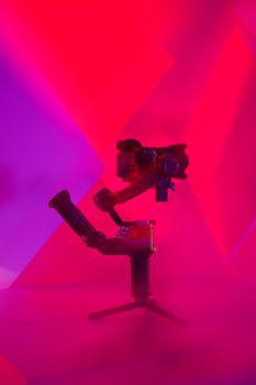 A gimbal-mounted camera with dramatic red and purple studio lighting, showcasing modern technology.