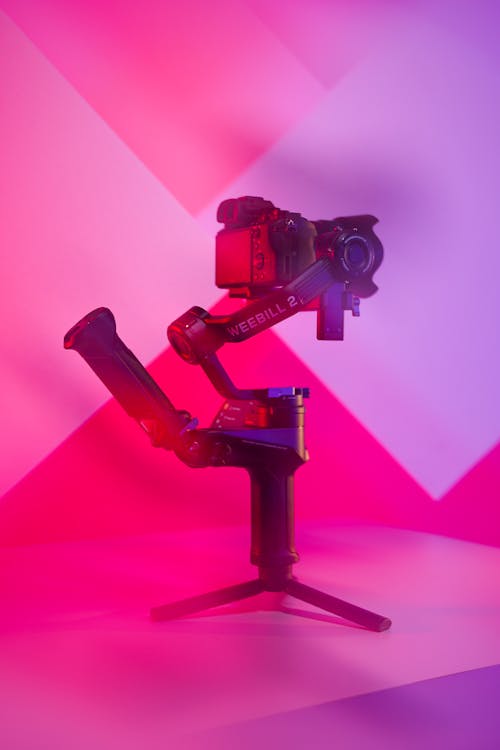 A camera on a tripod with a pink and purple background
