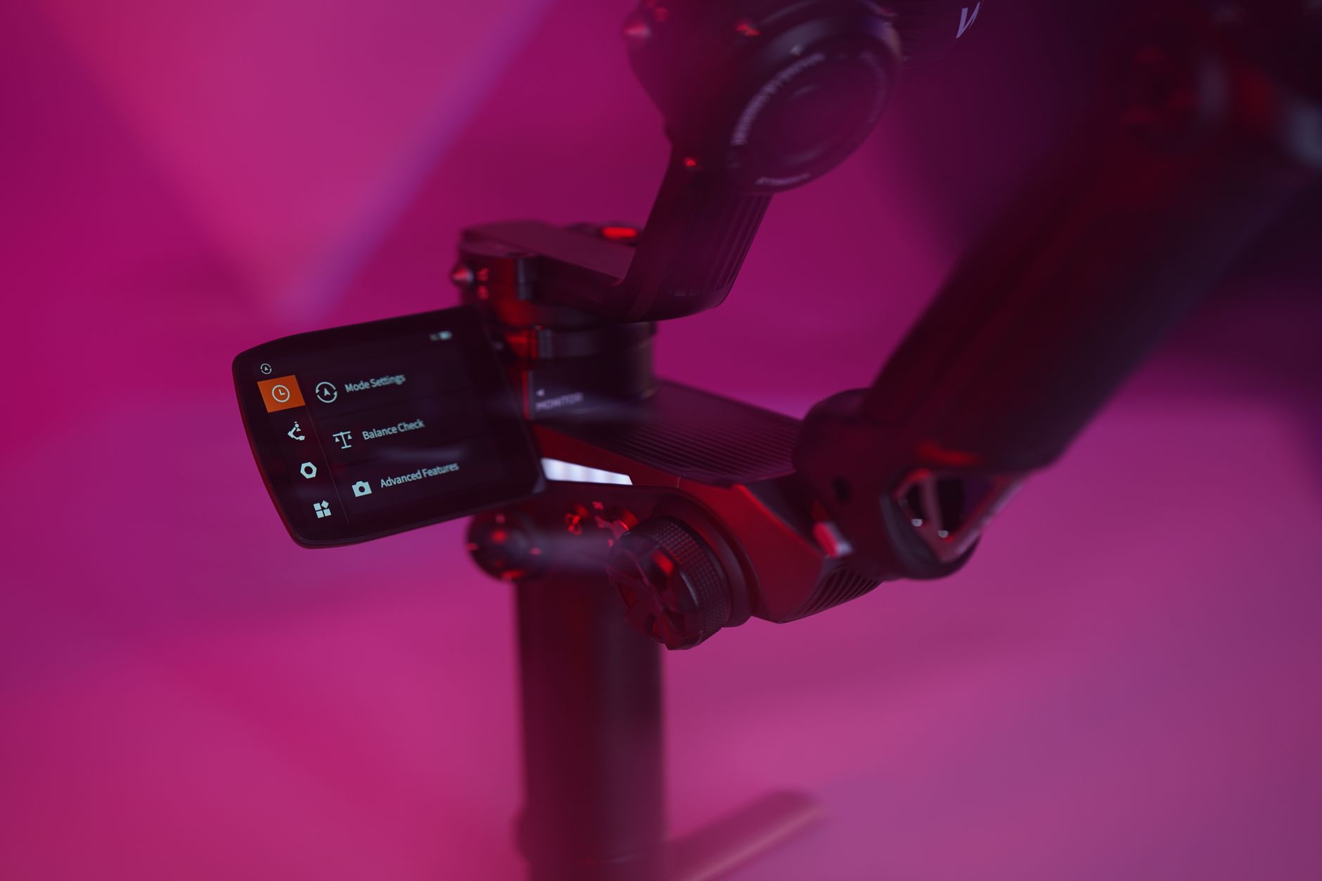 Detailed view of a camera gimbal with lit screen in a vibrant studio setting.
