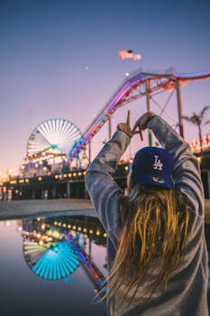 Back view of a woman enjoying Santa Monica Pier amusement park at twilight, reflecting vibrant lights. by Roberto Nickson