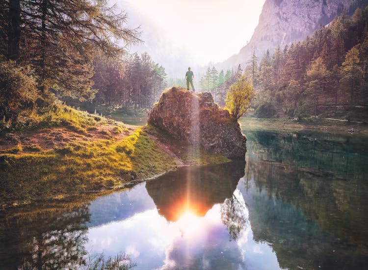 Photo Of Person Standing On Rock Near Lake