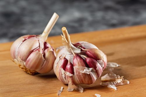 Free Close-up of fresh garlic bulbs resting on a wooden cutting board. Ideal cooking ingredient. Stock Photo