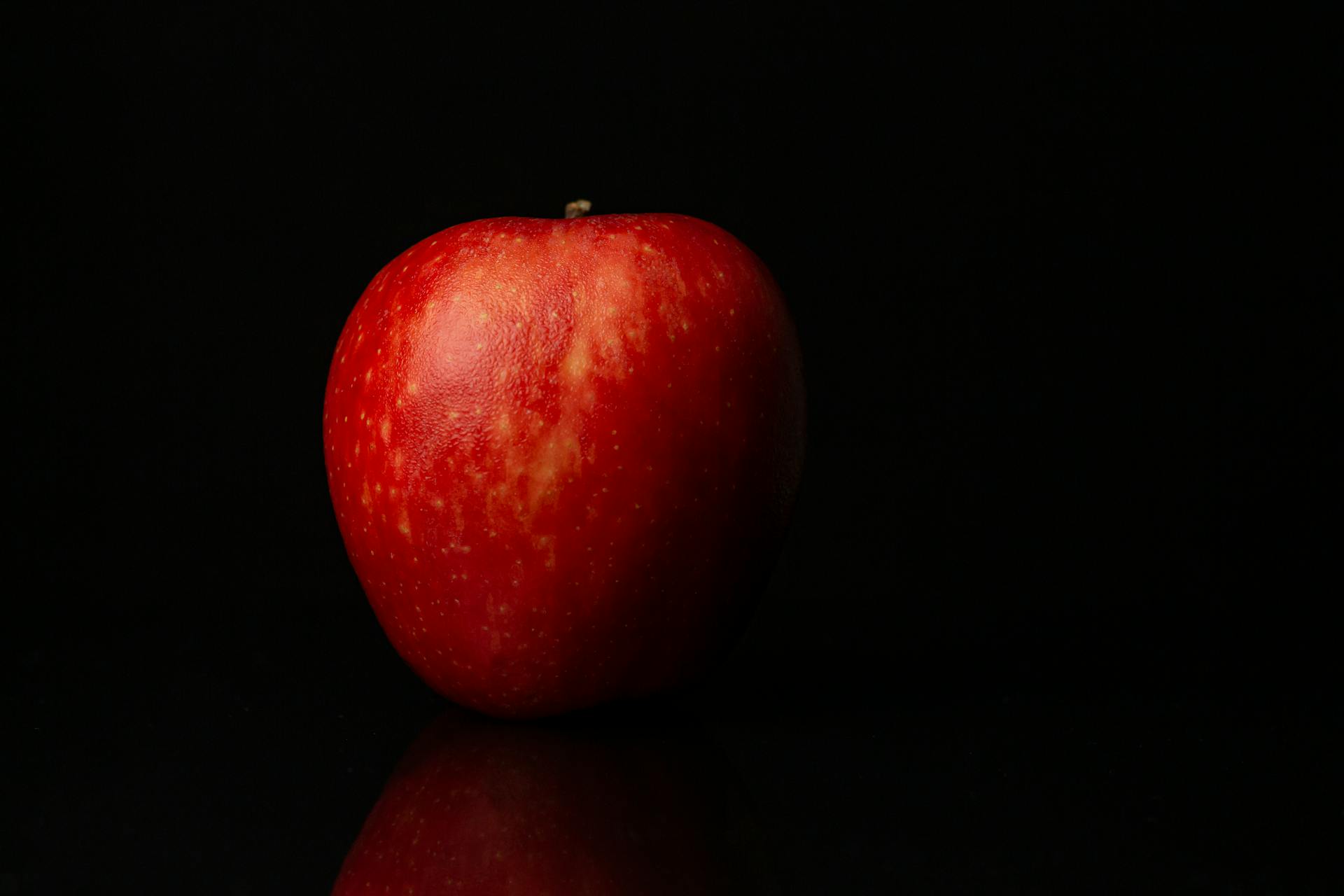 Detailed close-up of a single red apple against a black background, highlighting its fresh and ripe appearance.