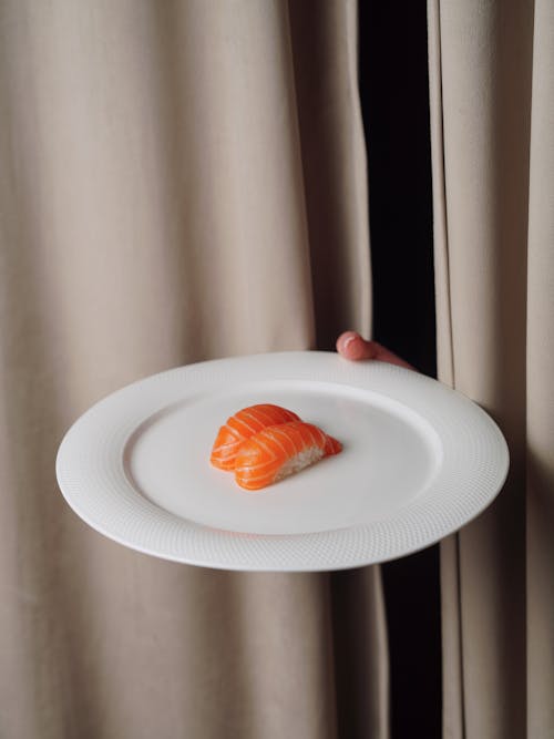 A person holding a plate with a piece of sushi