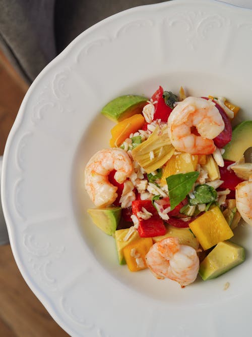 A white plate with shrimp, avocado and vegetables