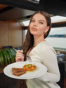 Stylish young woman in a white dress enjoying a gourmet meal indoors.