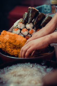 Close-up of hands preparing assorted sushi rolls with rice, fish, and seaweed wraps.