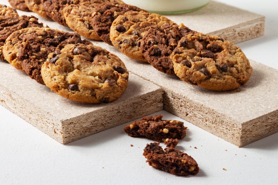 A wooden board with an assortment of sweet treats including chocolate chip cookies, caramel candies, mini tarts, and truffles dusted with cocoa powder.