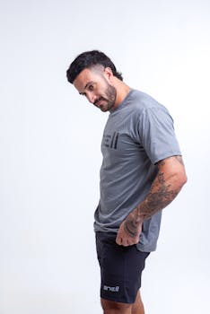 Portrait of a tattooed man in casual gray t-shirt and shorts against a white background.