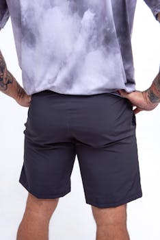 Back view of a tattooed man in shorts and gray t-shirt against a white background.