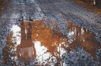 泥泞的未铺道路上的水坑中，映着鞋子和人的倒影