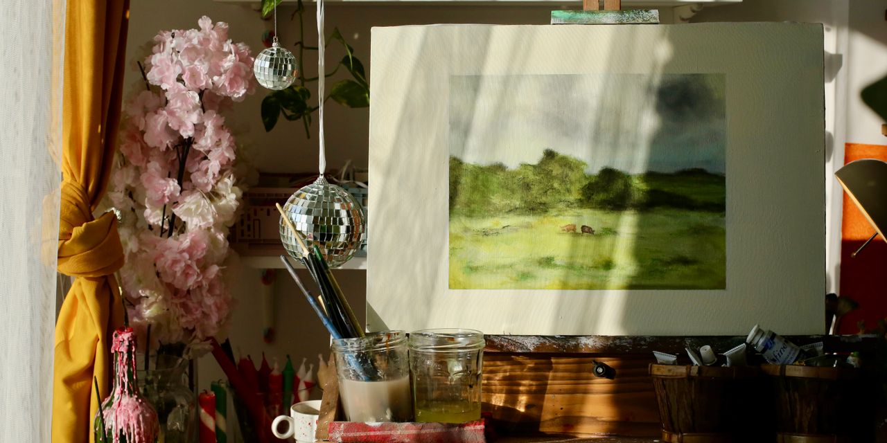 Sunlit art studio with painting supplies, easel, and a landscape artwork, evoking creativity.