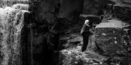 Monochrome Photography of Person Standing Near Rock Formation