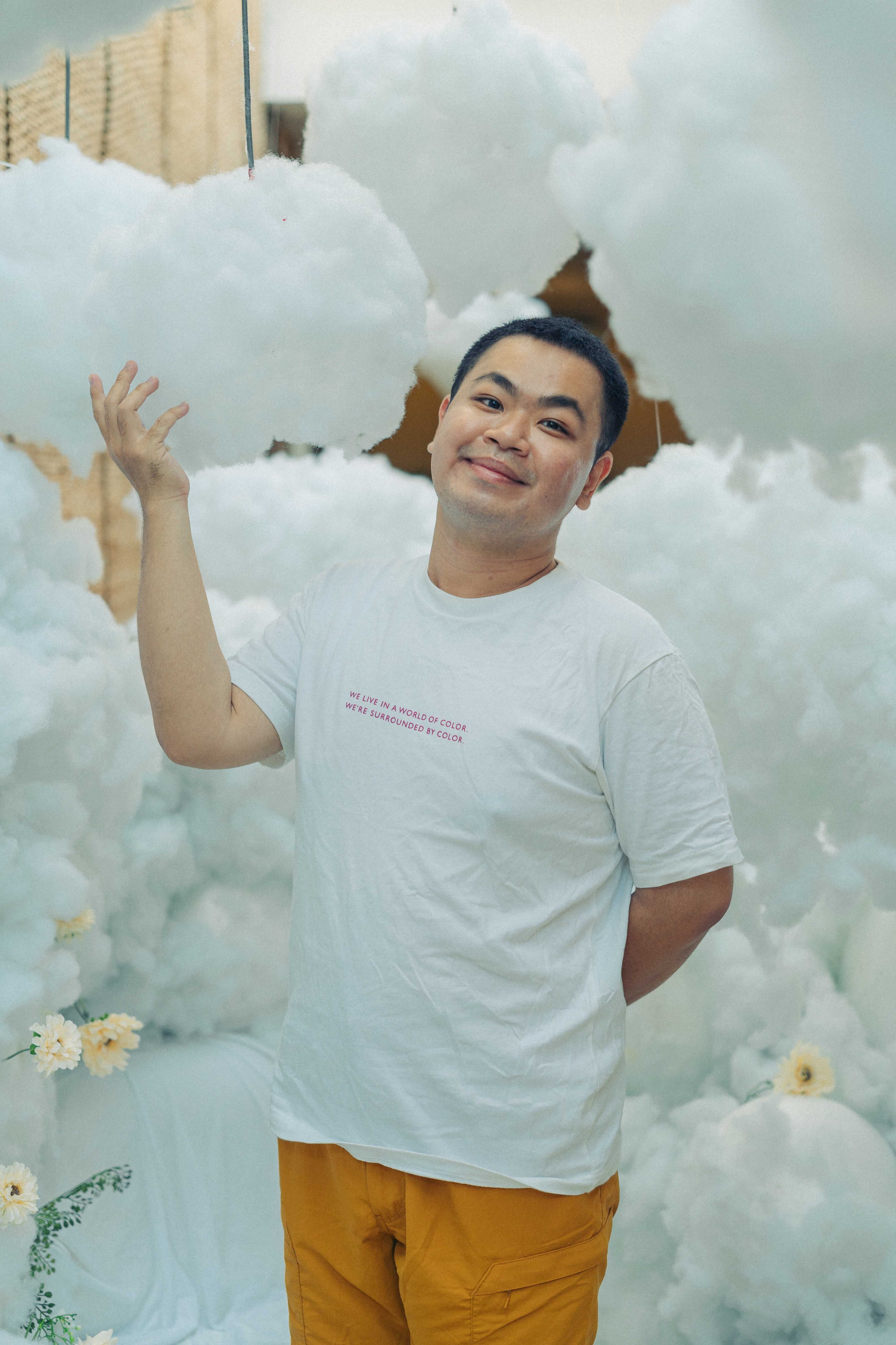 Smiling man posing with floating cotton clouds, creating a whimsical, imaginative ambiance.