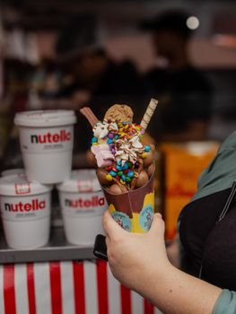 Close-up of a hand holding a vibrant ice cream dessert topped with candy, photographed indoors.