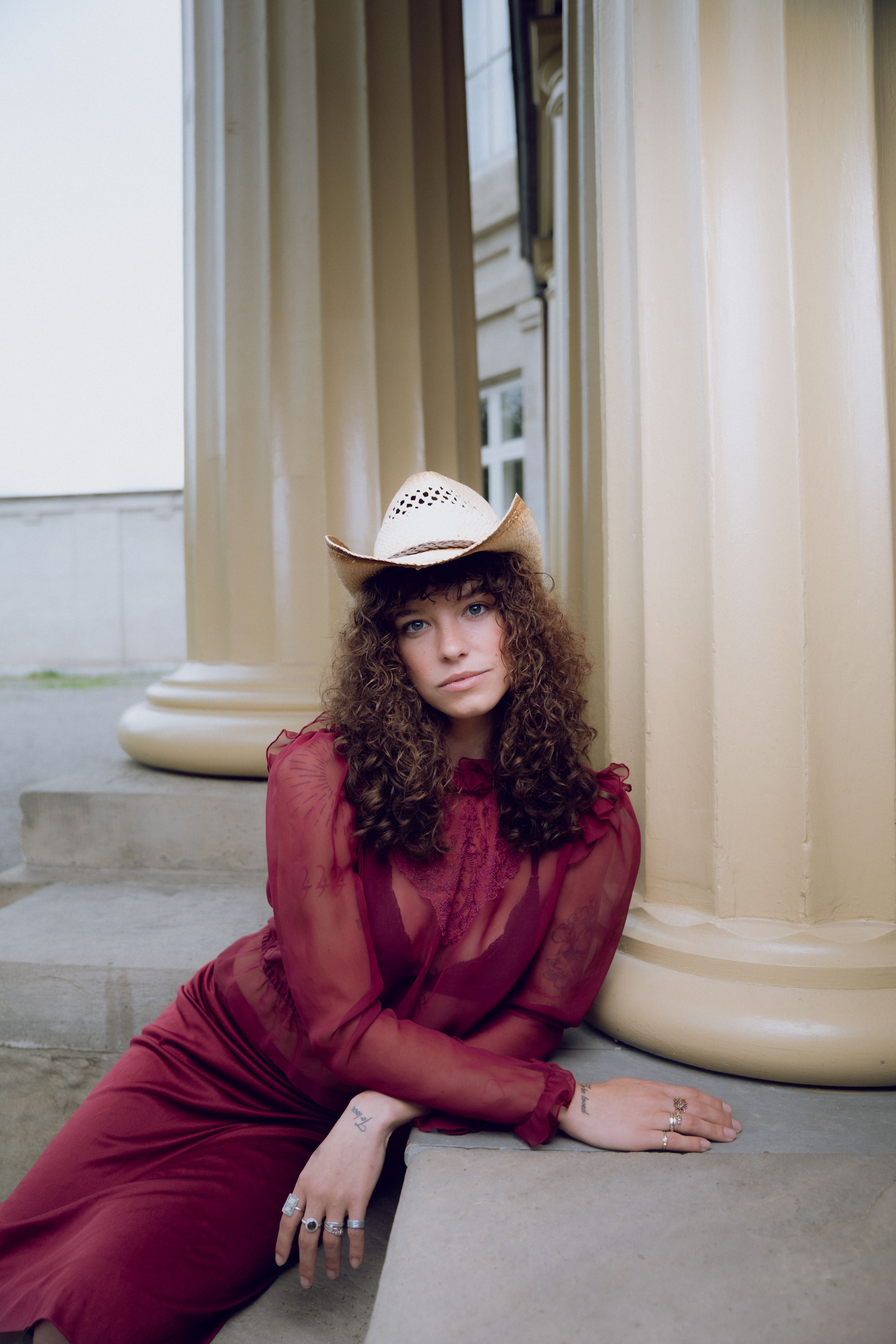 A woman in a red dress and hat sitting on a pillar · Free Stock Photo