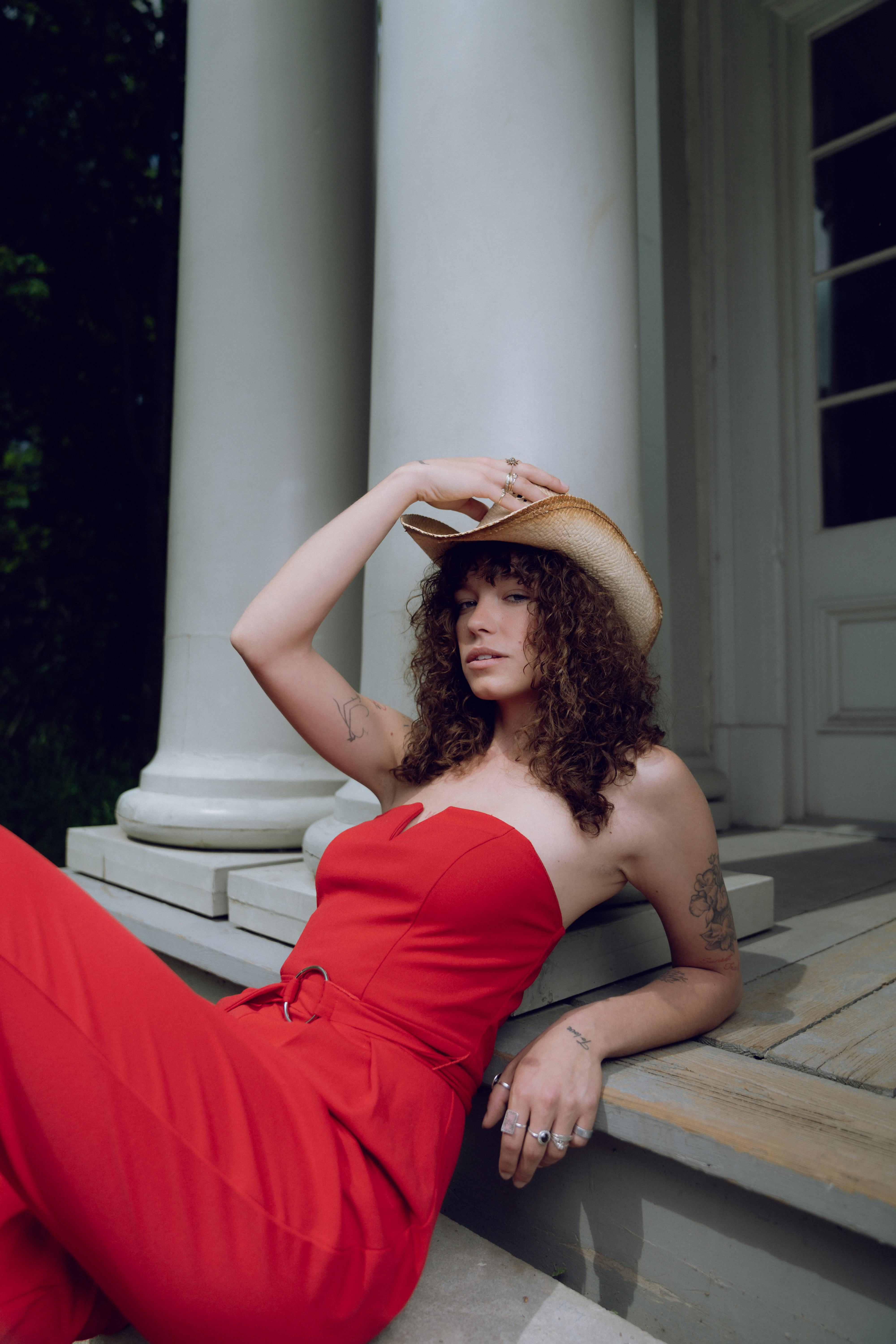 a woman in a red dress and hat sitting on a porch