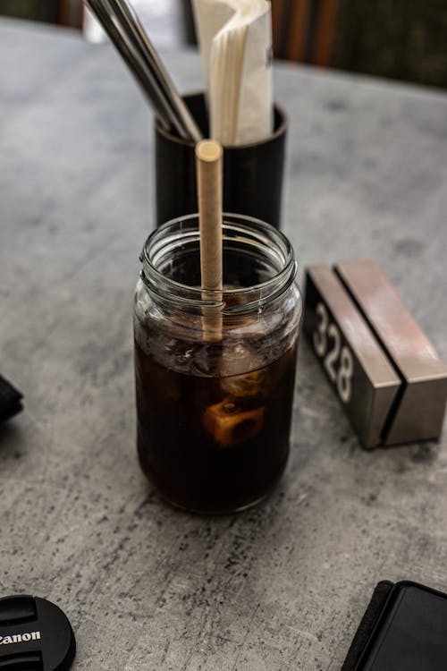 A jar of iced coffee with a straw and a wooden stick
